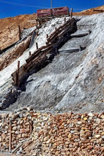 A lonely mine car stands on a rocky slope, surrounded by staggered layers of rock and wooden beams,