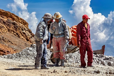 A group of miners stand and chat in a rocky landscape, The miners of the Cerro Rico silver mountain