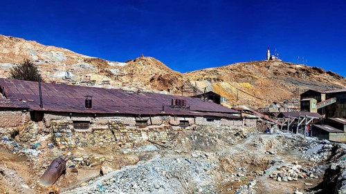 Old, dilapidated mining structures in front of a dry hill under a clear sky, The silver mines of