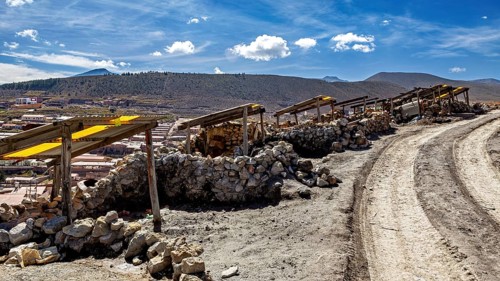 A dirt track leads through a dry, stony landscape under a blue sky with clouds, The silver mines of