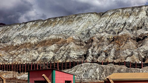 Industrial landscape with buildings at the foot of steep rock faces under a cloudy sky, slag heap