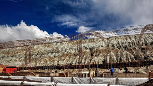 Industrial scene with scaffolding in front of a barren rock formation under a blue sky, slag heap