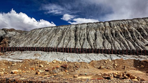 Steep rock faces in a barren desert landscape with clouds in the sky, spoil heap of the silver