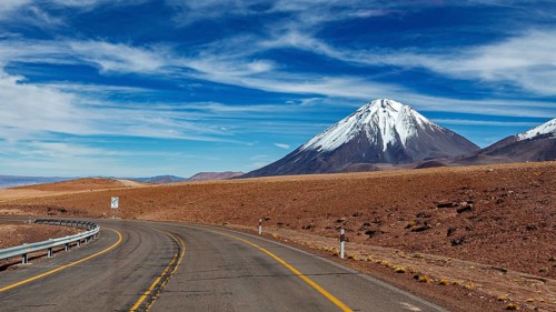 Deserted road leads to a snow-covered mountain under a clear sky, The landscape with the volcanoes