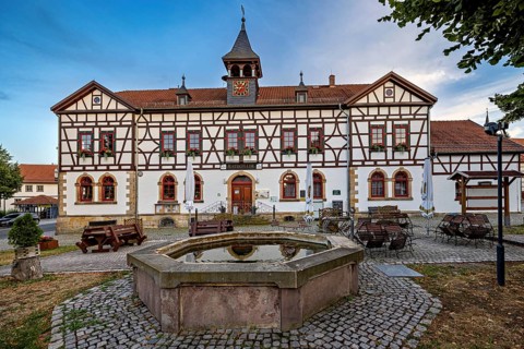 Half-timbered building with fountain and seating on cobblestone square at dusk, Historic