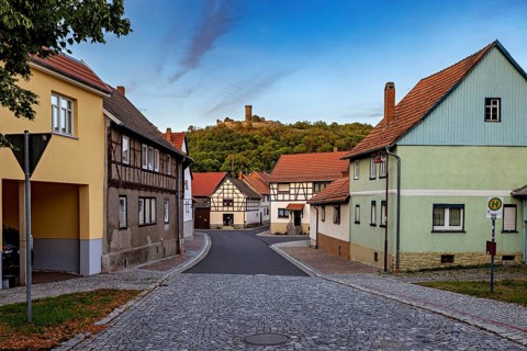 Historic village with half-timbered houses, castle ruins on a green hill and cobbled street, the