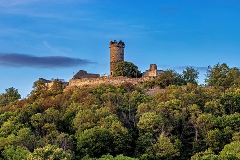 A castle with a tower on a wooded hill under a blue sky, the Mühlburg ruins one of the Drei