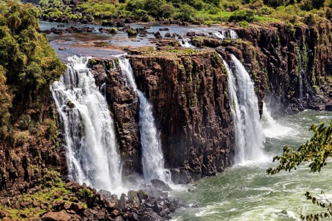Wide waterfalls cascade over steep cliffs into a bubbling river, The Iguazu Falls between Argentina