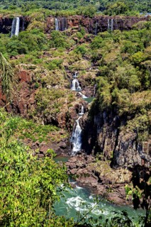A narrow waterfall meanders through rocky terrain, surrounded by dense vegetation, The Iguazu Falls