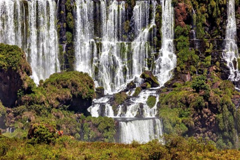 Several waterfalls cascade along jagged rocks, flanked by lush greenery, The Iguazu Falls between