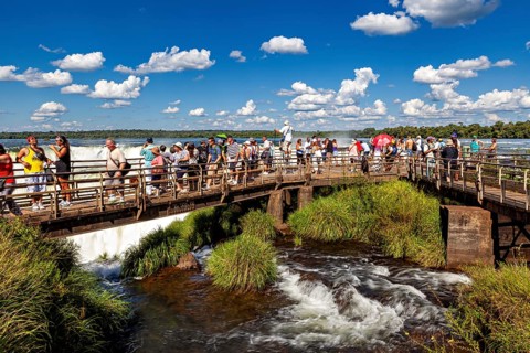 Group of tourists on a wooden bridge over a river with blue sky and clouds, tourist jetty at the