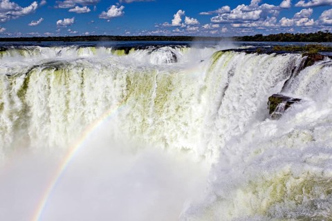 Waterfall with a rainbow over the foaming spray against a cloudy sky, The Iguazu Falls between
