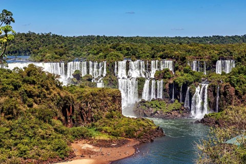 Lush waterfalls in a dense forest landscape with clear skies, The Iguazu Falls between Argentina