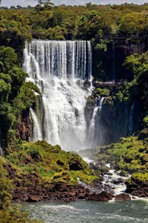 A large waterfall plunges into a river surrounded by dense foliage and rocks, The Iguazu Falls