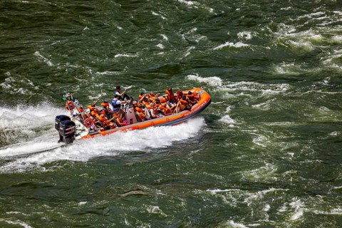 People in an orange-coloured rubber dinghy navigate through turbulent river waters, tourists in a