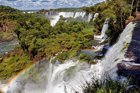 River course with waterfalls and rainbow in a lush forest landscape under a cloudy sky, The