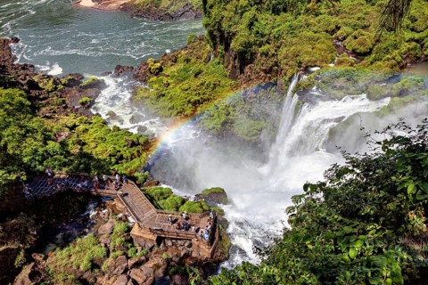 Visitors marvel at the waterfall from a platform above a rainbow on the riverbank, The Iguazu Falls