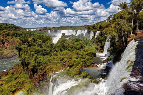 Several magnificent waterfalls and rainbows amidst lush vegetation under clear skies, The Iguazu