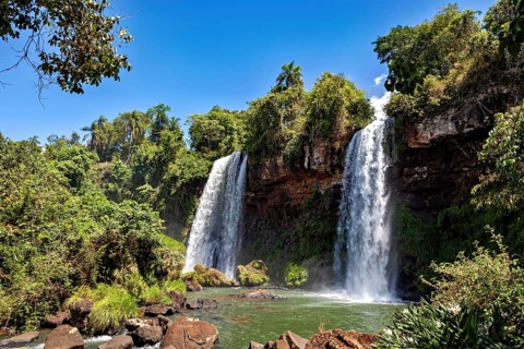 Two waterfalls pouring down amidst dense vegetation and bright sunshine, The Iguazu Falls between