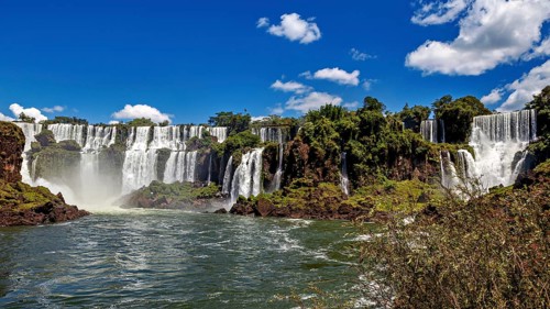 Majestic waterfalls with splashing water surrounded by green vegetation and blue sky, The Iguazu