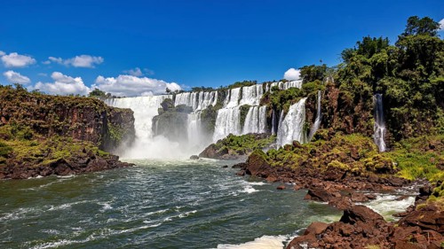 Impressive waterfalls with cascading floods and lush vegetation under a blue sky, The Iguazu Falls