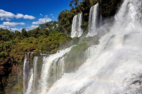 Waterfalls with dense fall and rainbow, embedded in lush forest under a blue sky, The waterfalls of