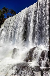 Close-up of a powerful waterfall with splashing spray and rocks under a blue sky, The Iguazu Falls
