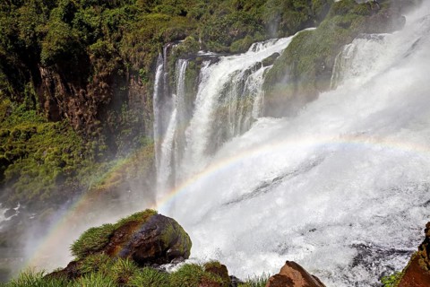 Powerful waterfall with spray and rainbow over mossy rocks in a natural setting, The Iguazu Falls