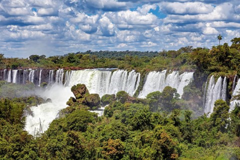 Expansive view of a large waterfall amidst lush green forests and cloudy skies, The Iguazu Falls