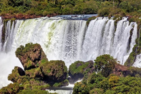 Large waterfall with lush vegetation and rocky ledges, The Iguazu Falls between Argentina and