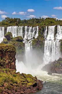 Impressive waterfalls cascade powerfully over rocks, surrounded by green vegetation and under a
