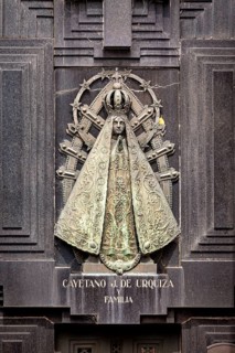 Metal relief of a Madonna on a dark stone surface with engravings and religious symbols, La