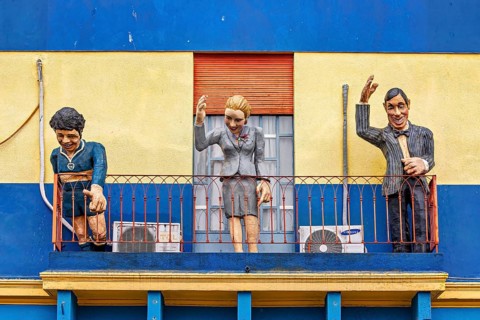 Three figures on a balcony of a historically painted building, The colourful city and tango
