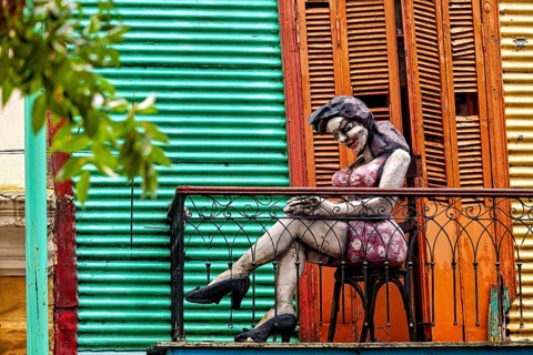 Sculpture of a woman on a balcony in front of a colourful façade, The colourful city and tango