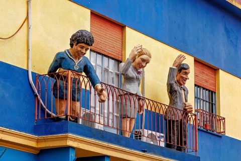 Figures on a balcony of a blue and yellow building in La Boca, the colourful city and tango