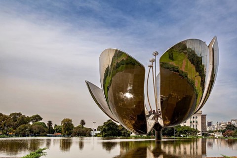 Large metal flower sculpture on the edge of a lake with a cloudy sky in the background, The lotus