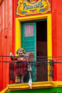 A humorous sculpture of a woman on a balcony in front of a colourful building, The colourful city
