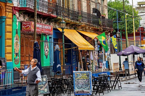 A lively street market with colourful banners and cafés, people stroll past, The colourful city and