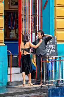 A couple discussing in front of a colourful entrance in tango clothes, the woman wears a black