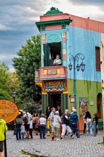 A lively place with colourful buildings and people, a statue stands on the balcony, The colourful