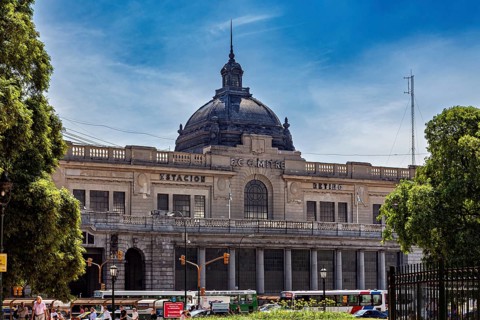 A large railway station with a dome, surrounded by trees and traffic under a blue sky, The city of