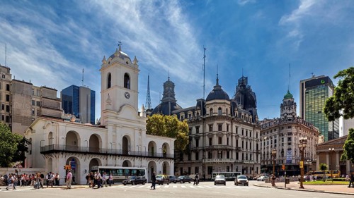 An architectural ensemble with historic buildings and a striking clock tower under a blue sky, The