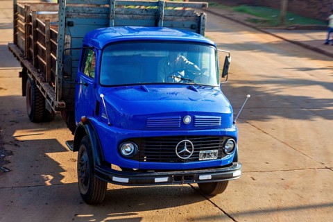 Blue Mercedes-Benz lorry on a sunny road, transporting wood, vintage style, An old Mercedes lorry