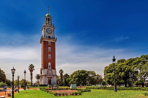 A clock tower surrounded by manicured gardens, palm trees and lanterns in a sunny park, The city of