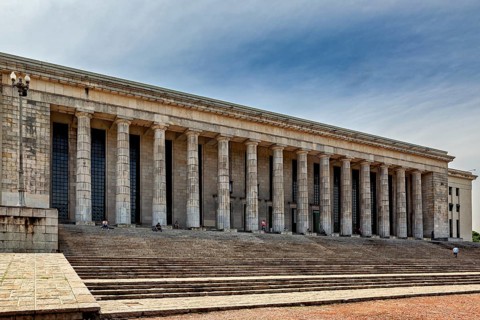 A wide building with many columns and large stairs in front of a slightly cloudy sky, The city of