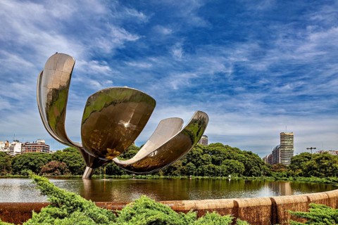 Imposing metallic flower with urban background, surrounded by a pond and trees, The lotus flower in
