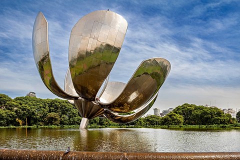Large metallic flower with reflective surface in a park with water and green foliage, The lotus