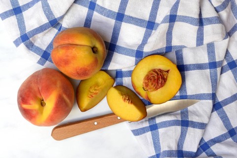 Peach with knife on kitchen towel, peach halves, Prunus persica