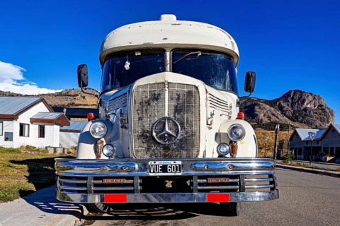Front view of a vintage bus with Mercedes-Benz logo, against a mountainous backdrop and clear sky,