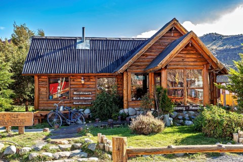 Cosy wooden house with a small garden, mountains behind it in the sunny daylight, the village of El